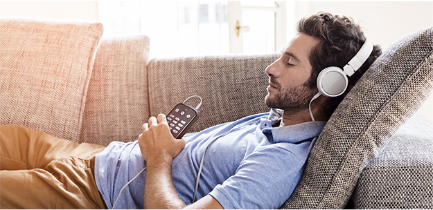 Man resting on a couch listening to an audio book