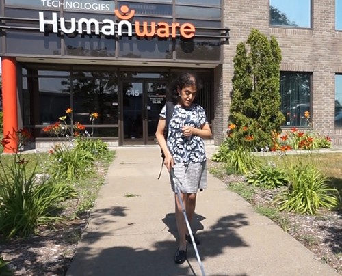 Photo of an intern leaving the HumanWare offices, using a white cane to guide herself.