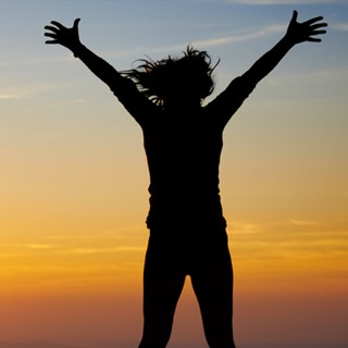 Image of a silhouette of a person with its hands in the sky against a sunset background.