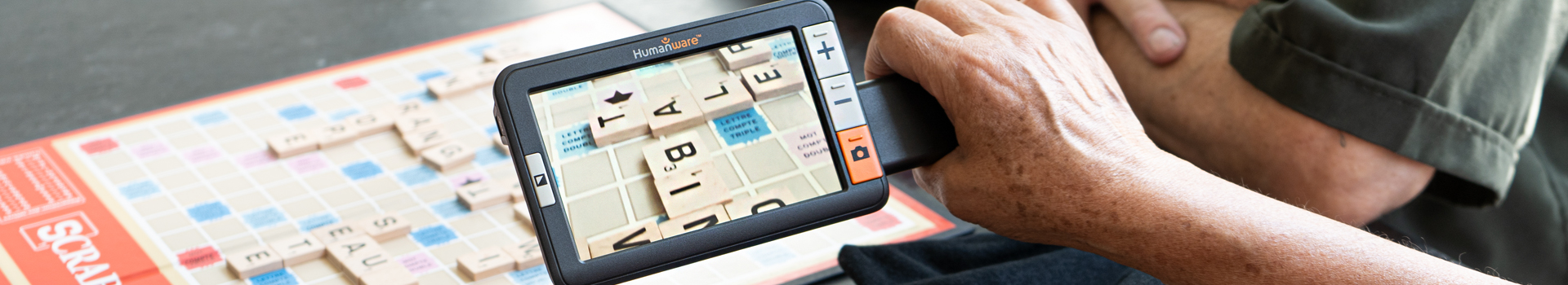 Image of two people playing Scrabble; one uses the exploré 5 to enlarge the board and letter tiles.