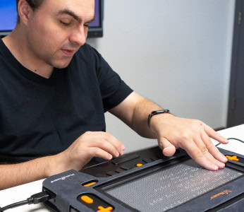 A man using a Monarch device to read braille, highlighting technological accessibility for individuals with visual impairments.