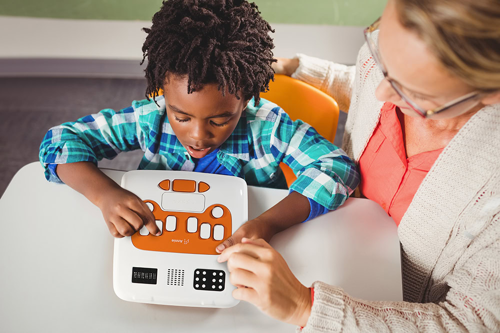 A child is using Annie, guided by an adult with blonde hair. The environment is bright, fostering interactive and attentive learning.