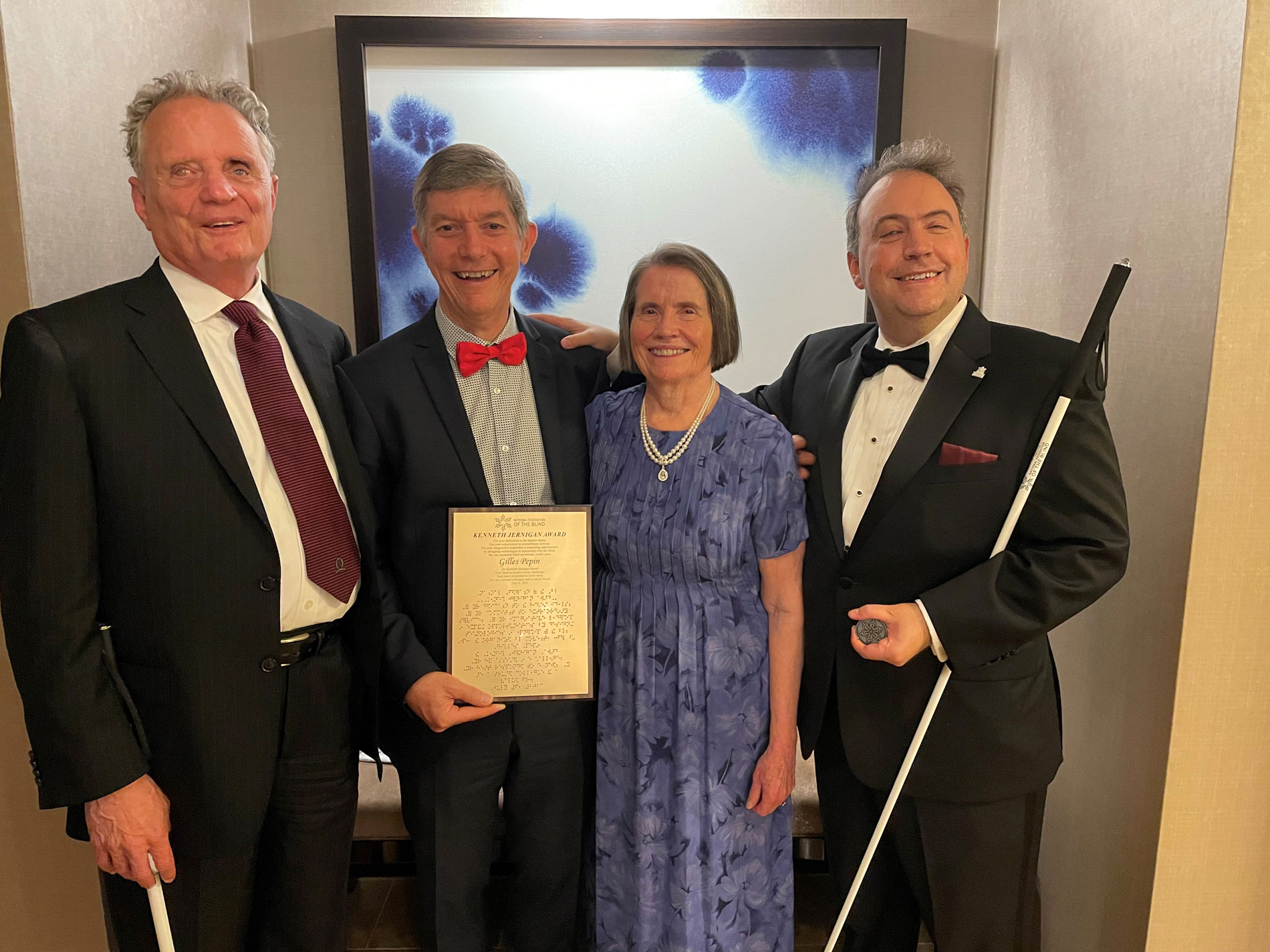 Group photo captured at the 2023 NFB National Convention, featuring Gilles Pepin proudly holding his well-deserved award joined by Dr. Marc Maurer, past NFB President, Mary Ellen Jernigan, the wife of the late Kenneth Jernigan, and Mark Riccobono, the current President of the NFB.