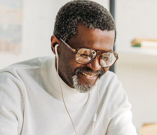 Image of a smiling adult male with gray hair and glasses using headphones with his audio assistant.