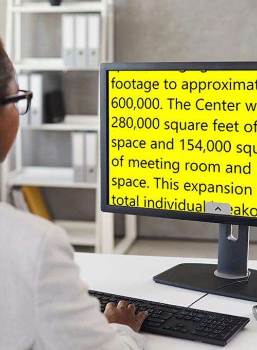 Image of a person seated at a desk, looking at a computer screen displaying high-contrast black text on a yellow background, related to an article about an expansion project.