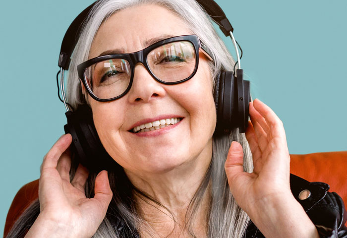 Image of a smiling adult woman with long white hair using headphones with her audio assistant.